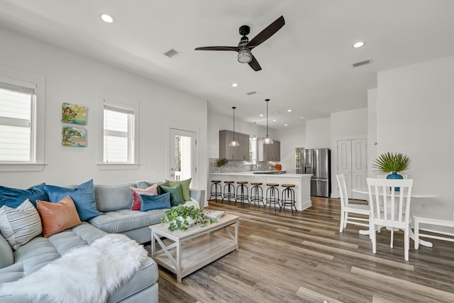 living area with a ceiling fan, recessed lighting, visible vents, and wood finished floors