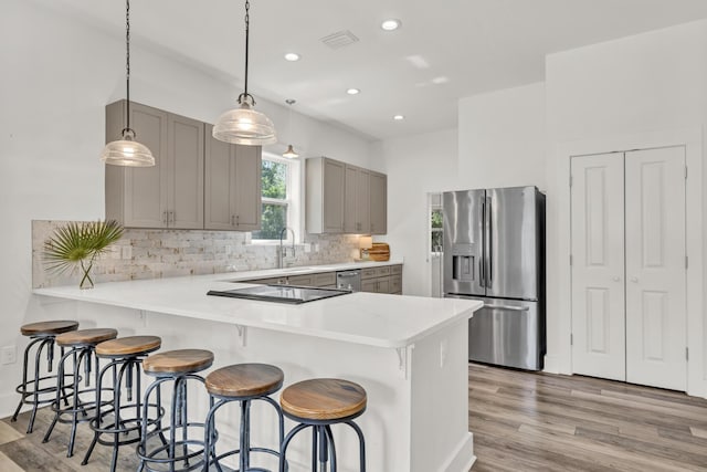 kitchen with a peninsula, light countertops, appliances with stainless steel finishes, backsplash, and gray cabinets