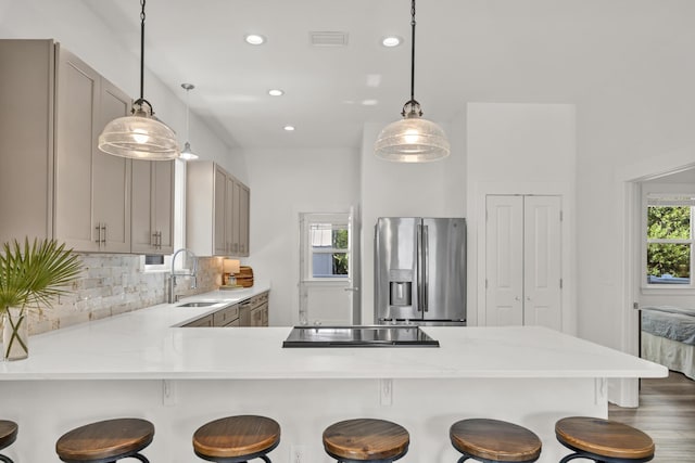 kitchen with cooktop, tasteful backsplash, a peninsula, stainless steel refrigerator with ice dispenser, and a sink