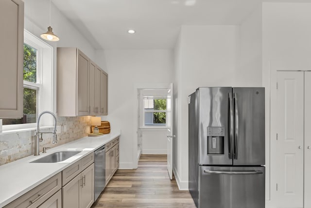 kitchen featuring decorative backsplash, stainless steel appliances, light countertops, light wood-style floors, and a sink