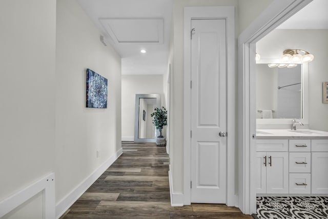 hallway featuring dark wood-style floors, attic access, baseboards, and a sink