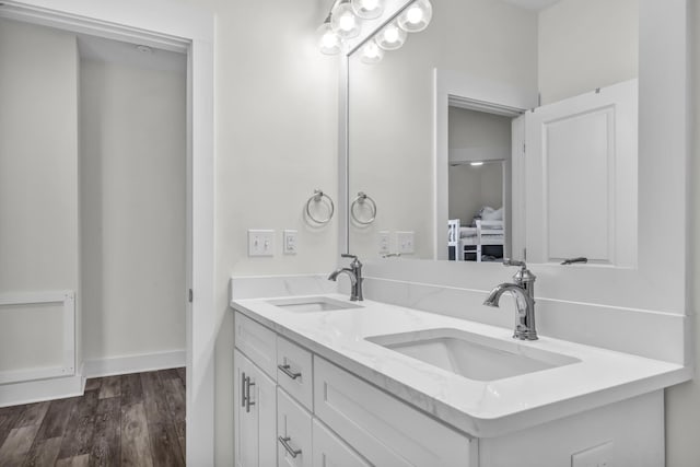 full bathroom with double vanity, wood finished floors, a sink, and baseboards