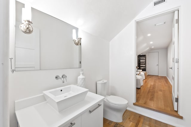 bathroom featuring toilet, wood finished floors, vanity, visible vents, and vaulted ceiling