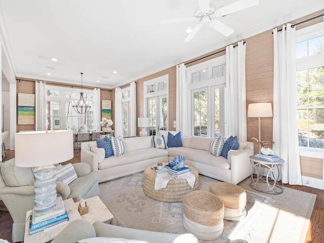 living room featuring ornamental molding, a wealth of natural light, ceiling fan with notable chandelier, and wood finished floors