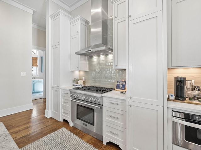 kitchen featuring backsplash, appliances with stainless steel finishes, ornamental molding, white cabinetry, and wall chimney exhaust hood