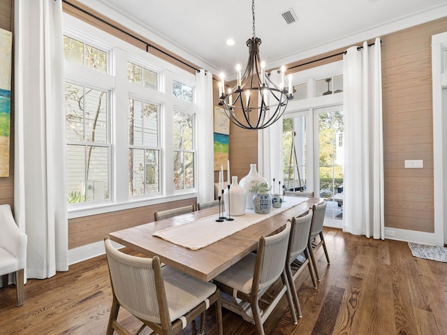 dining area with crown molding, visible vents, dark wood-type flooring, wood walls, and a chandelier