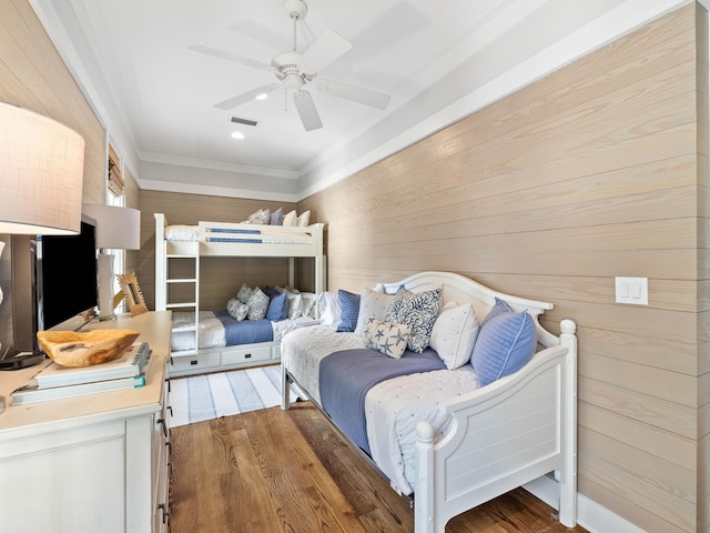 bedroom featuring ceiling fan, wood walls, dark wood-style flooring, visible vents, and crown molding