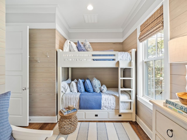 bedroom featuring wooden walls, baseboards, visible vents, ornamental molding, and dark wood-type flooring