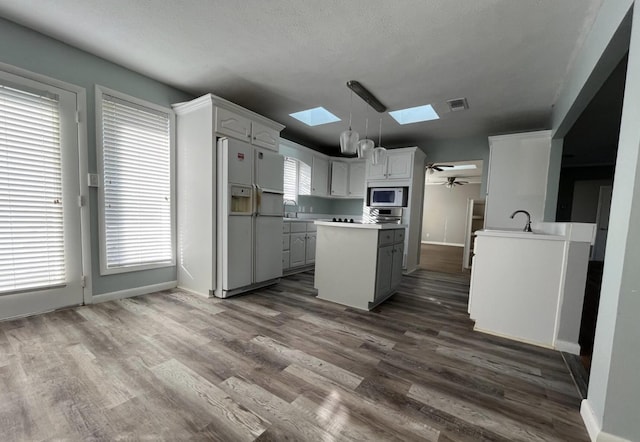 kitchen featuring built in microwave, white cabinetry, a skylight, pendant lighting, and white refrigerator with ice dispenser