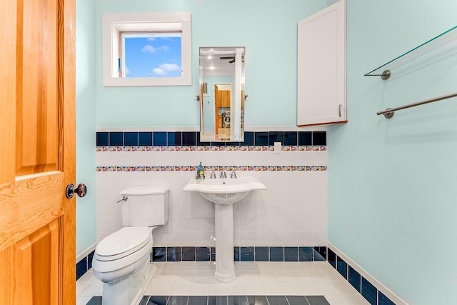 bathroom featuring a wainscoted wall, tile walls, toilet, and tile patterned floors