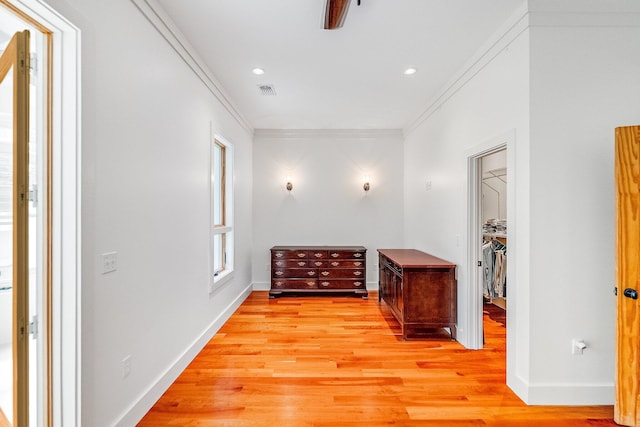 hall with baseboards, light wood-style floors, visible vents, and crown molding