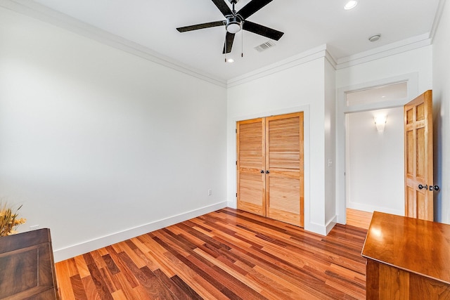 unfurnished bedroom featuring wood finished floors, visible vents, baseboards, ornamental molding, and a closet