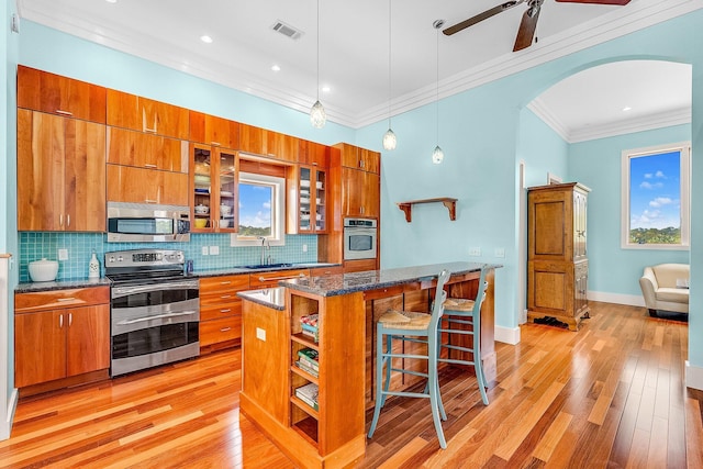 kitchen featuring a breakfast bar area, stainless steel appliances, visible vents, brown cabinetry, and a sink