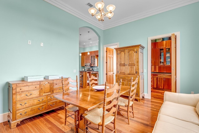 dining area with visible vents, arched walkways, ornamental molding, light wood-style floors, and a notable chandelier