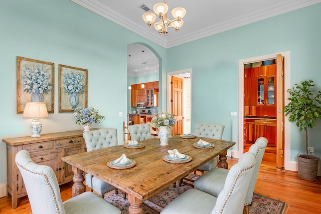 dining space featuring arched walkways, crown molding, visible vents, light wood-style flooring, and an inviting chandelier