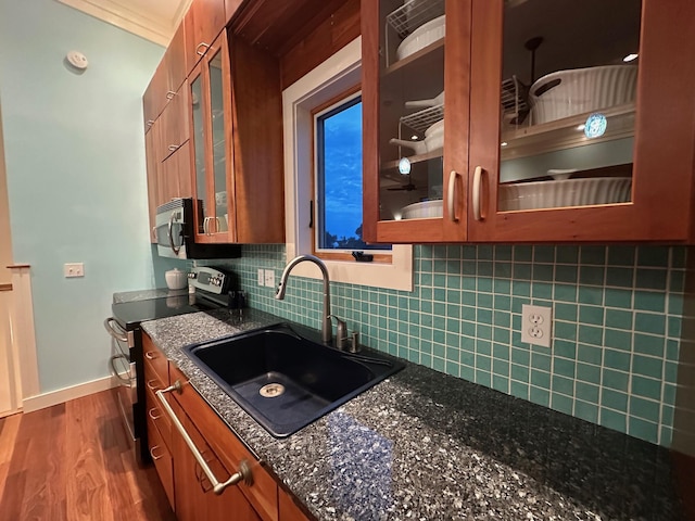 kitchen with dark wood-type flooring, a sink, appliances with stainless steel finishes, decorative backsplash, and brown cabinetry