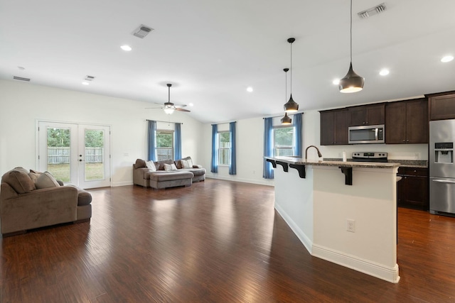 kitchen featuring dark brown cabinetry, stone countertops, a center island with sink, appliances with stainless steel finishes, and a kitchen breakfast bar