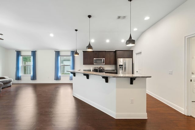 kitchen with dark wood-type flooring, a kitchen bar, dark brown cabinets, stainless steel appliances, and a center island with sink