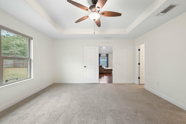 carpeted spare room featuring a tray ceiling and ceiling fan