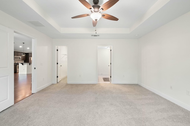 unfurnished room with ceiling fan, carpet flooring, and a tray ceiling