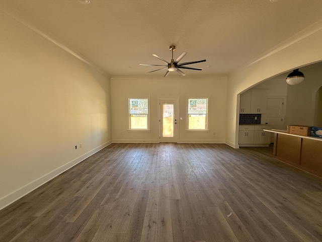 unfurnished living room featuring dark wood-style floors, ornamental molding, a ceiling fan, and baseboards