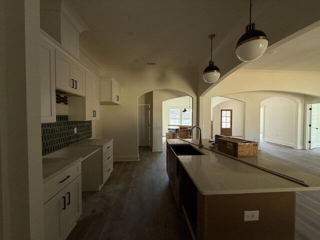 kitchen with arched walkways, backsplash, white cabinetry, a sink, and wood finished floors