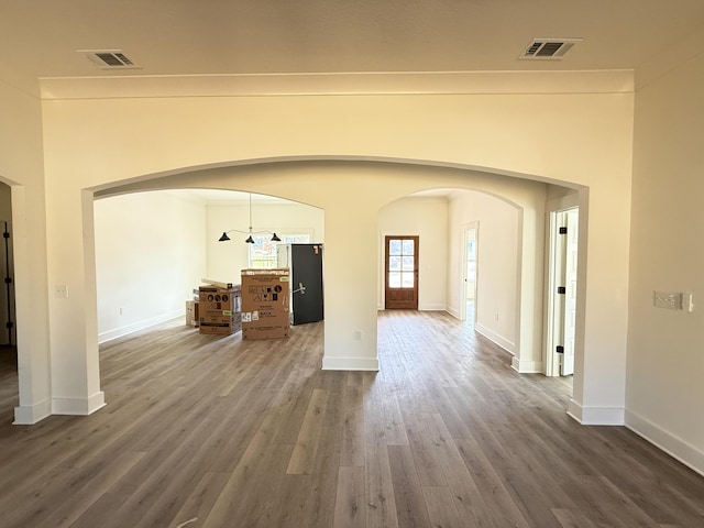 unfurnished living room featuring baseboards, visible vents, arched walkways, and wood finished floors