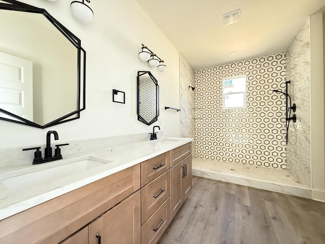 bathroom featuring a textured ceiling, a walk in shower, a sink, and wood finished floors