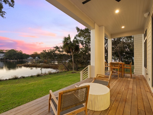 deck at dusk featuring a water view and a lawn