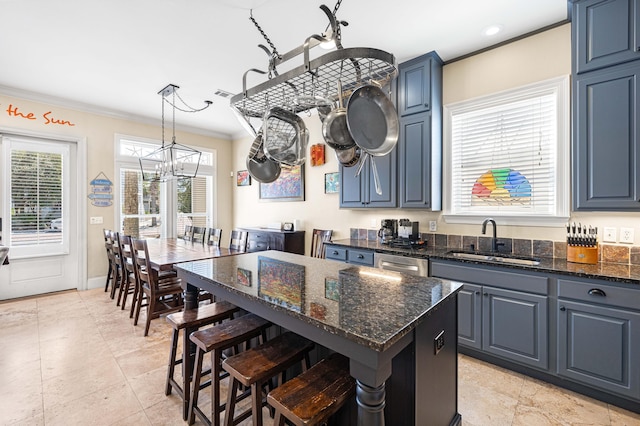 kitchen featuring dark stone counters, a breakfast bar area, a sink, crown molding, and a notable chandelier