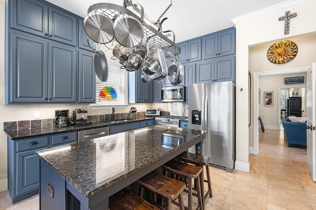 kitchen with appliances with stainless steel finishes, a breakfast bar, a center island, blue cabinets, and a sink