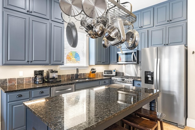 kitchen featuring dark stone counters, a breakfast bar, stainless steel appliances, blue cabinetry, and a sink