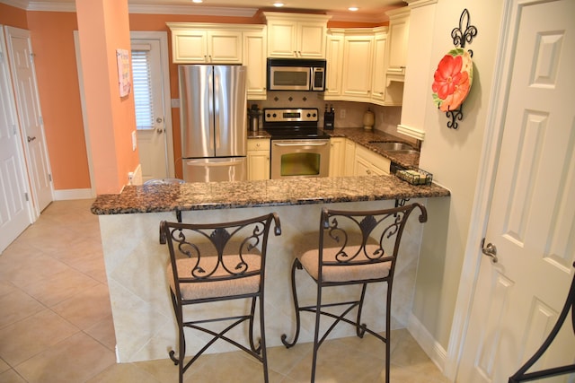 kitchen with stainless steel appliances, crown molding, dark stone countertops, and kitchen peninsula