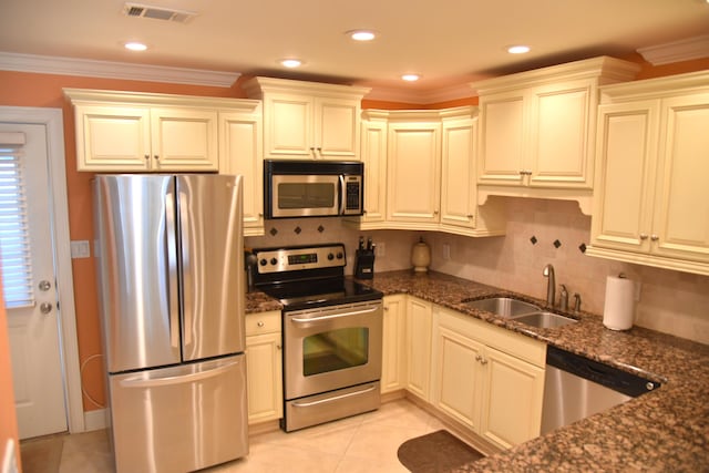 kitchen featuring appliances with stainless steel finishes, sink, dark stone countertops, ornamental molding, and light tile patterned floors