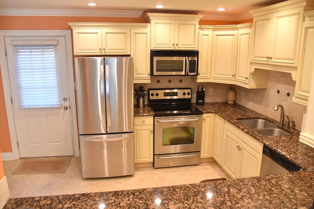 kitchen featuring sink, light tile patterned floors, dark stone countertops, ornamental molding, and stainless steel appliances