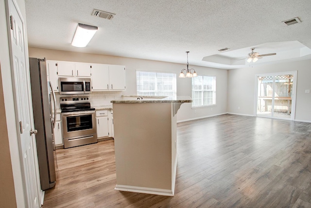 kitchen featuring pendant lighting, appliances with stainless steel finishes, white cabinetry, light stone counters, and a raised ceiling