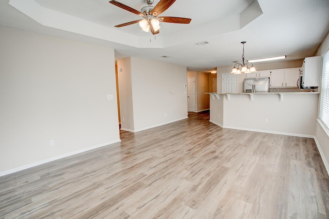 unfurnished living room featuring a tray ceiling, ceiling fan with notable chandelier, and light wood-type flooring