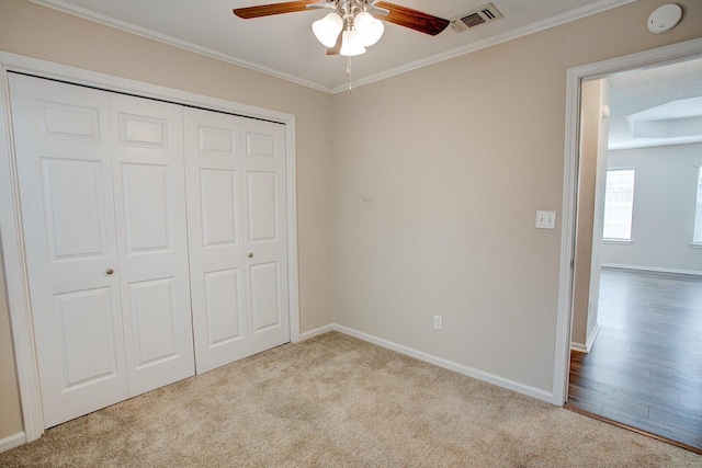 unfurnished bedroom with ornamental molding, light colored carpet, ceiling fan, and a closet