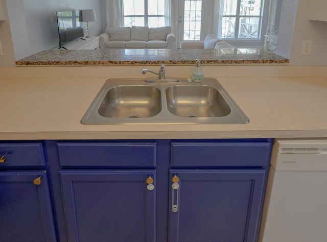 kitchen featuring blue cabinetry, a sink, open floor plan, white dishwasher, and light countertops