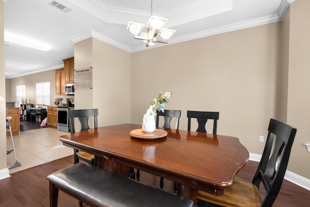 dining area featuring crown molding, a notable chandelier, light wood finished floors, a raised ceiling, and visible vents