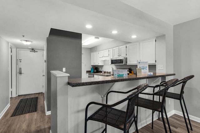 kitchen with white cabinetry, hardwood / wood-style floors, a kitchen bar, and kitchen peninsula