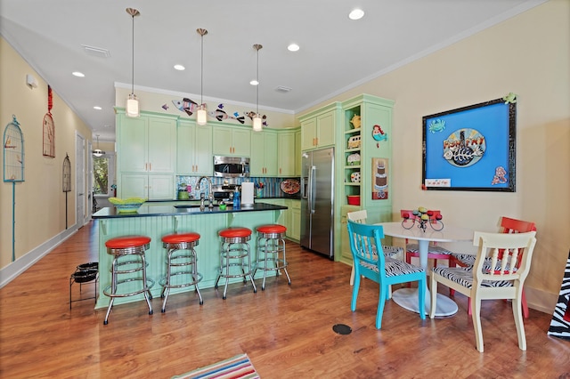kitchen with appliances with stainless steel finishes, wood-type flooring, sink, hanging light fixtures, and an island with sink