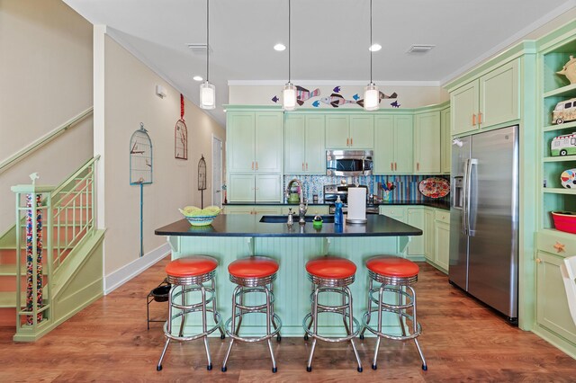 kitchen featuring hardwood / wood-style floors, an island with sink, stainless steel appliances, and decorative light fixtures