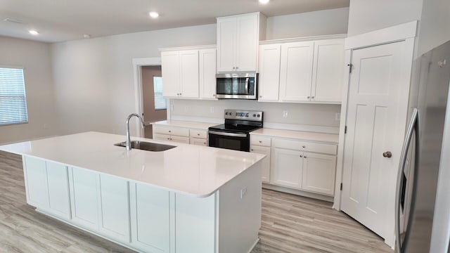 kitchen featuring light wood finished floors, a center island with sink, appliances with stainless steel finishes, white cabinetry, and a sink