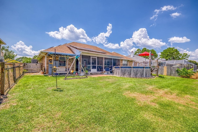 back of property with a fenced in pool, a sunroom, a fenced backyard, a yard, and brick siding