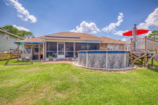 rear view of house with a sunroom, a fenced in pool, solar panels, and a yard