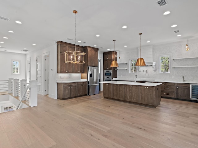 kitchen featuring appliances with stainless steel finishes, decorative light fixtures, a kitchen island with sink, and light wood-type flooring