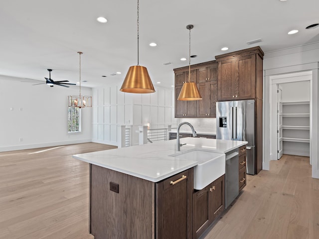 kitchen with sink, light stone counters, decorative light fixtures, a center island with sink, and appliances with stainless steel finishes