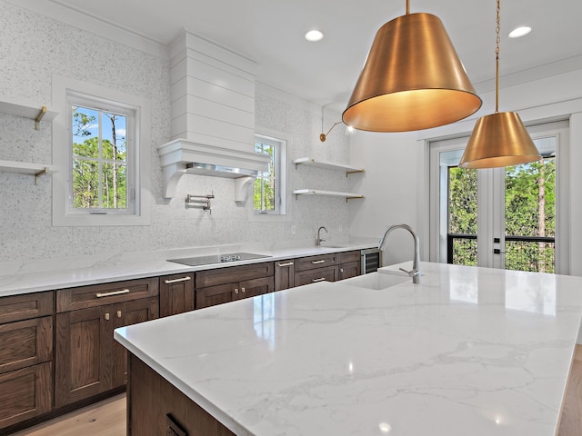 kitchen featuring light stone counters, sink, black electric cooktop, and a center island with sink