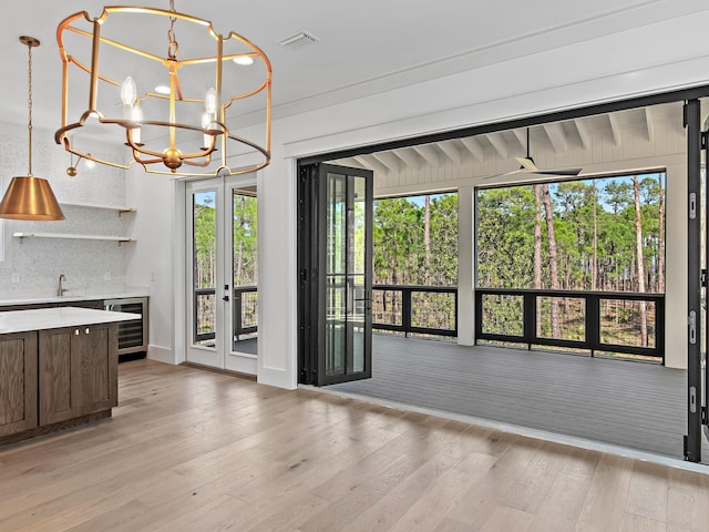 unfurnished dining area featuring sink, light hardwood / wood-style flooring, beverage cooler, a chandelier, and french doors